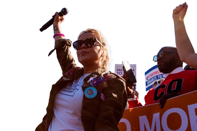 A woman raising a microphone in the air with additional protesters 