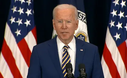 President Biden giving a speech in front of a pair of American flags