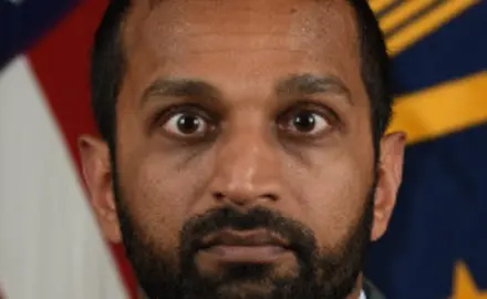 Kash Patel pictured in front of an American flag staring intensely at the camera