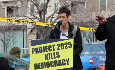 Rally speaker in front of a sign that reads "Project 2025 kills democracy"