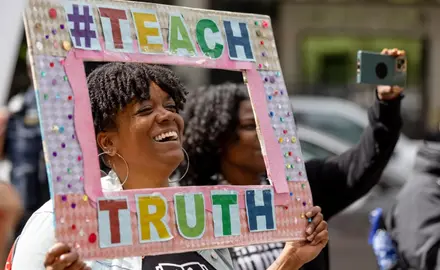 Woman holding a sign framing her face  that says #TeachTruth