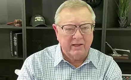 Image of Tim Sheets, a post-middle-age white man wearing glasses, sitting with bookshelf behind him  