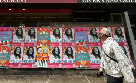 A man walks by a wall of posters of Kamala Harris that say Freedom