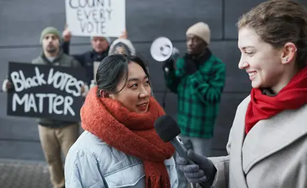 A reporter with a microphone interviews voting rights protestors