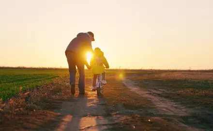 Dad teaching a daughter to ride a bike on a dirt road