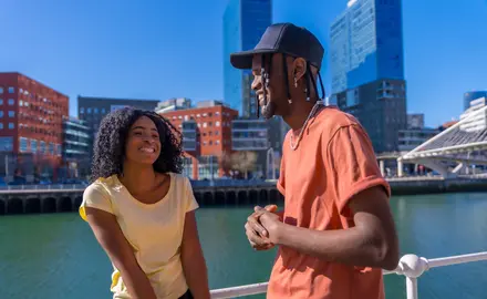 Photo of a young Black man and woman walking along a body of water in a city