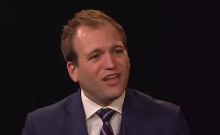 Image taken from video: Johnnie Moore in suit and tie against dark background, speaking to off-camera CBN hosts.