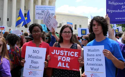 three people holding pfaw signs at a rally in front of supreme court