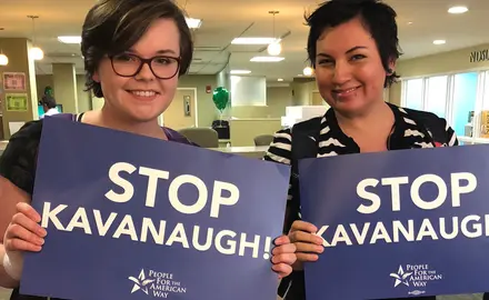 Two smiling students hold blue signs that say Stop Kavanaugh.