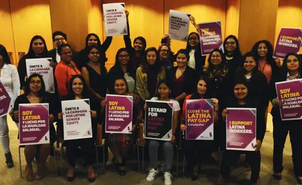 A group of people holding signs that say "Close the Latina pay gap" "I support Latina workers" and "Soy latina"