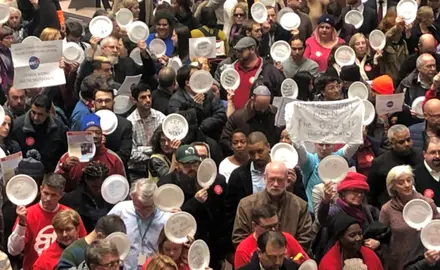 A crowd of people hold paper plates in a rally