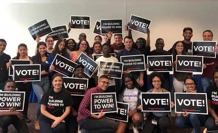 A group of people holding signs that say "Vote" and wearing tee-shirts that say "I'm building the power to win!"