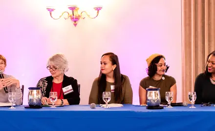 A group of multicultural women sit on a panel.