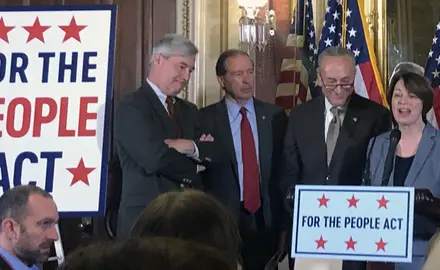 Amy Klobuchar stands at a podium next to Sens. Whiteshouse, Schumer, and Merkley to introduce the For the People Act