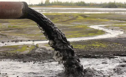 A pipe dumps grey sludge into the environment