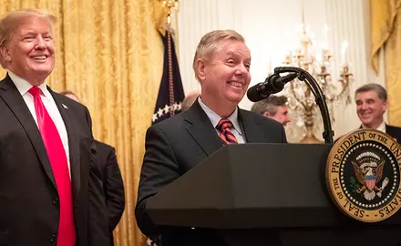 Lindsey Graham stands behind a podium with Donald Trump at his side.