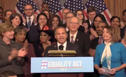 Rep. David Cicilline speaks at a podium with a group of applauding Congresspeople