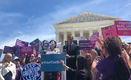 Senator Blumenthal and Representative Chu stand at a podium surround by activists at a #StoptheBans rally