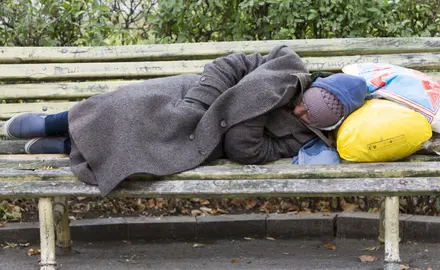 A homeless person naps with their belongings on a bench