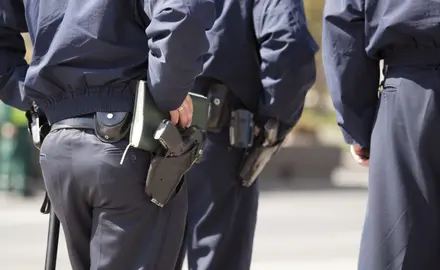 A close-up of police officers waists with guns on their hips