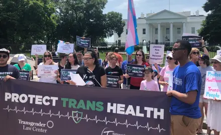 A group of activists stand outside the White House holding signs demanding that the administration "Protect Trans Health" and "Protect healthcare for trans people."