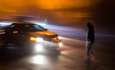 A person crosses the street in front of a car.