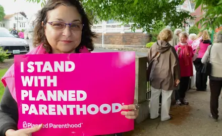 A woman holds a pink sign that says "I stand with Planned Parenthood"