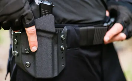 A close up of a police officer's belt; the officer has his hand on his gun