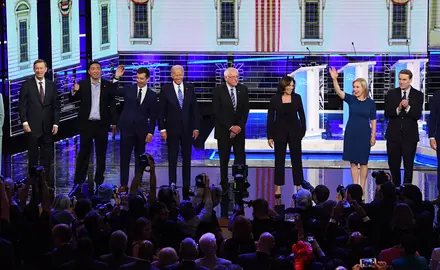 The Democratic presidential candidates smile and wave from the front of the stage at the second debate.