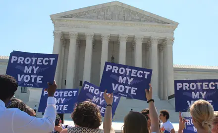 Six people hold up blue signs that read 'protect my vote' at a rally in front of the supreme court