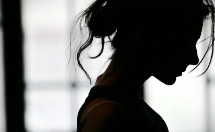 A somber black silhouette of a woman with messy hair looking down.