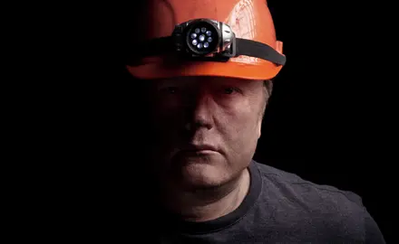 A man wearing an orange hard hat with a headlamp attached