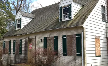 A boarded up house with a notice on the front door.