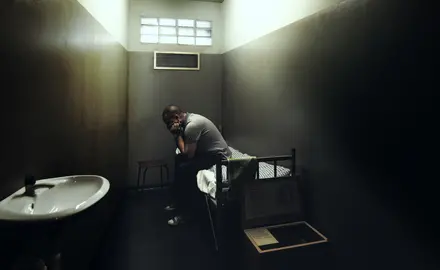 A man in solitary confinement sits on his bed in a small cell.