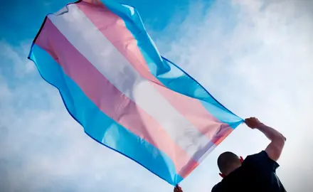 A man holds the transgender flag above his head.