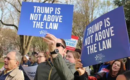 Activists hold signs saying "Trump is not above the law."