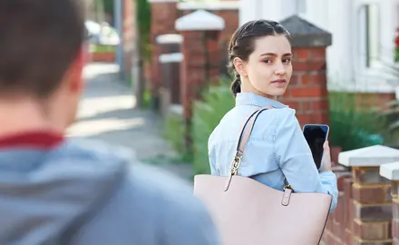 A woman holding her phone looks over her shoulder at the man following her