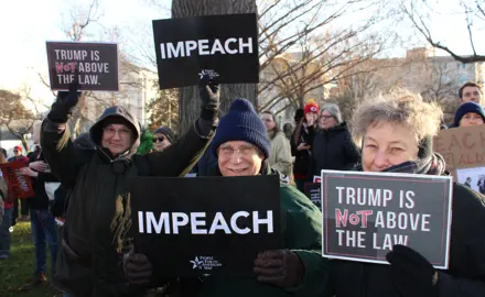 Activists hold signs calling for Donald Trump's impeachment and removal.