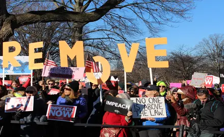 A group of rally-goers hold signs stating "Impeach now," "Impeach," and "No one is above the law" outside the Capitol Building in December 2019.