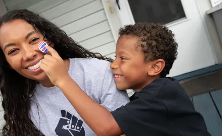 A Black son places an "I Voted" sticker on his mother's smiling face.