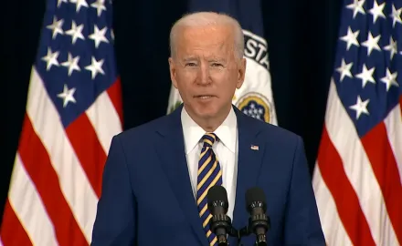 President Joe Biden stands in front of several American flags.