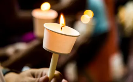 Hands holding candles with paper wax protectors.