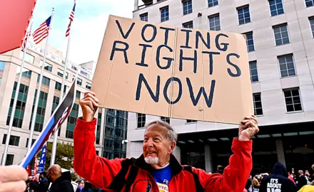 A man holds a cardboard sign that reads Voting Rights Now