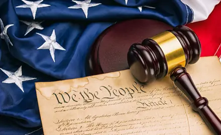 Picture of an American Flag and the U.S. Constitution with the phrase "We The People" clearly visible underneath a gavel.