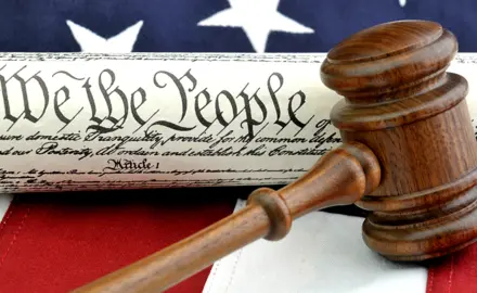 Picture of an American Flag and the U.S. Constitution with the phrase "We The People" clearly visible underneath a gavel.