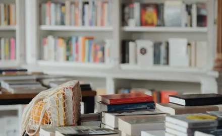 A table full of books in the foreground and shelves of books in the background.