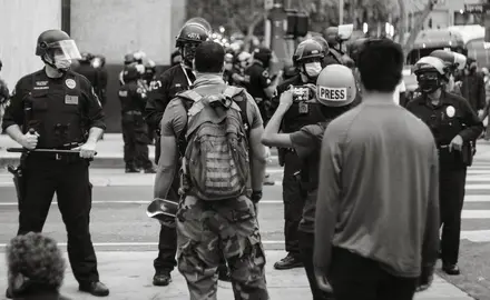 Two Black men and a reporter face a line of police in riot gear.