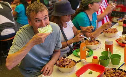 Phil Rosenthal sits at a table with several women eating food.