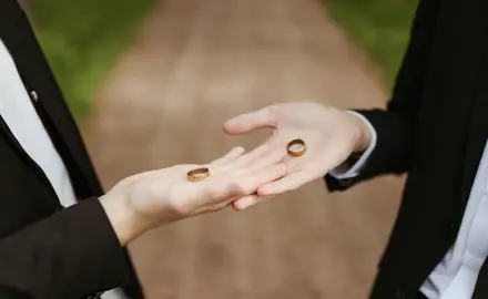 Two hands each holding a wedding ring in their palms.