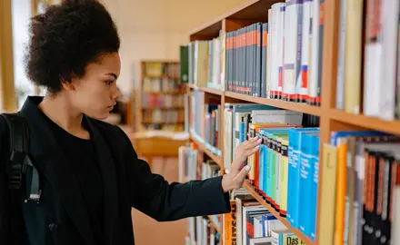 A Black woman looks at a shelf of books in a school library.